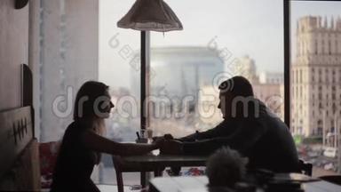 一对情侣坐在桌旁约会的剪影。 高楼大厦咖啡厅窗外的城市街景不错。